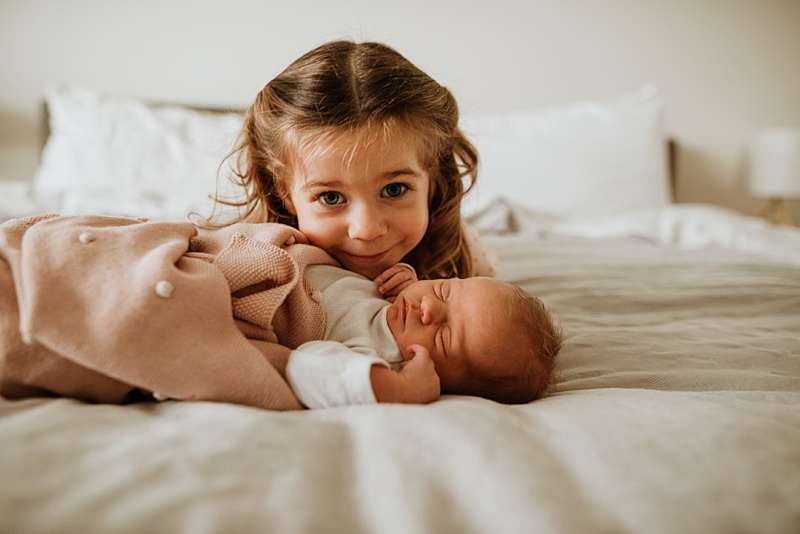 Big sister and baby sister snuggling. Here are my 5 tips for older siblings at newborn sessions.