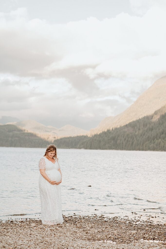 pregnant woman wearing a white gown for a maternity photography session near a lake in Vancouver BC