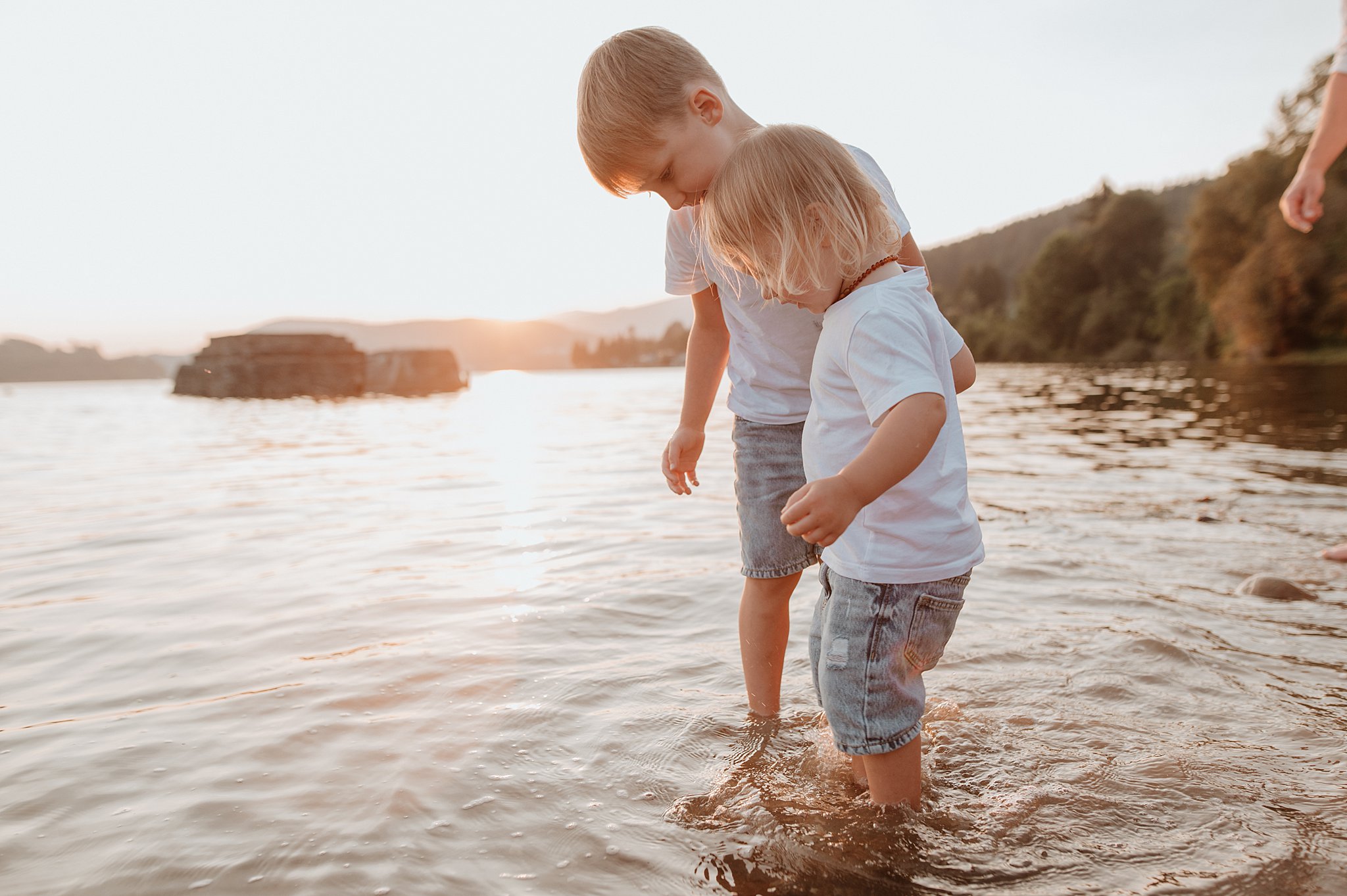 Two young toddler brothers explore some shallow river water in jean shorts and white shirts after visiting vancouver daycares