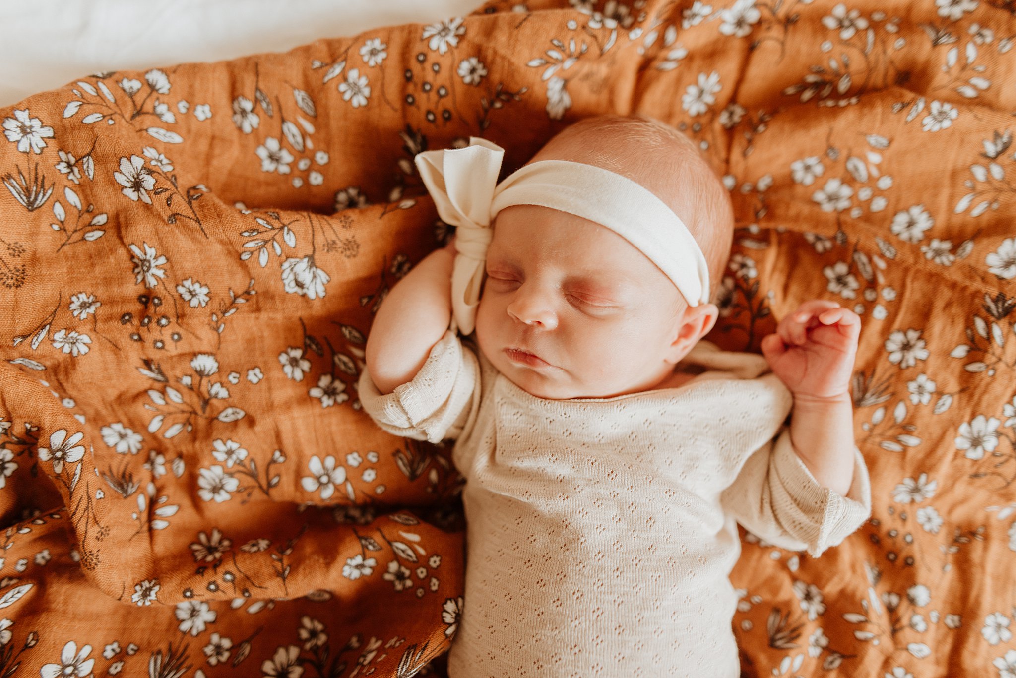 A newborn baby girl sleeps in mom's lap in a large bow headband on an orange floral dress thanks to vancouver diaper service