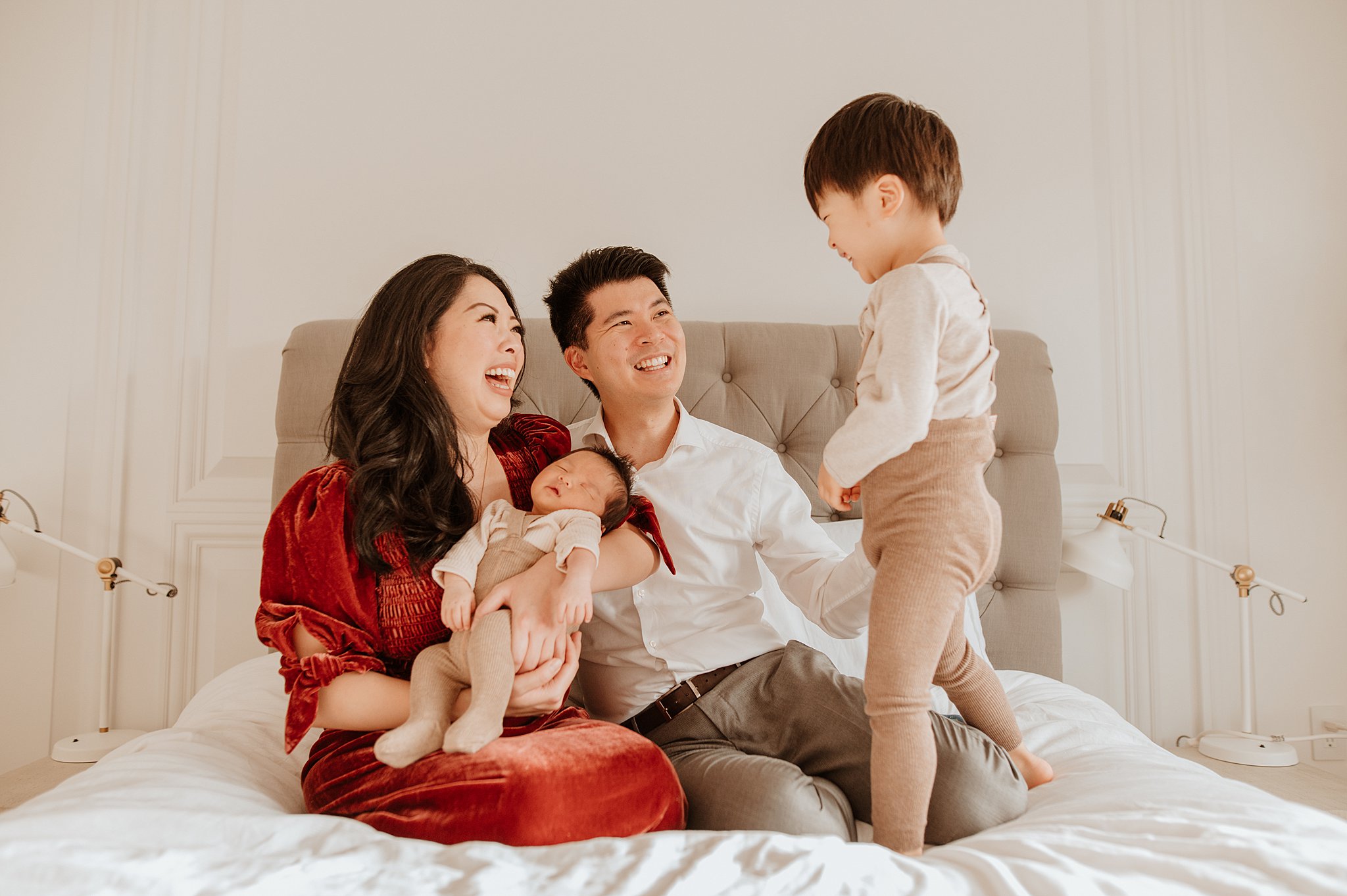 A mom and dad sit on a bed holding their sleeping newborn baby and playing with their toddler son thanks to vancouver prenatal massage