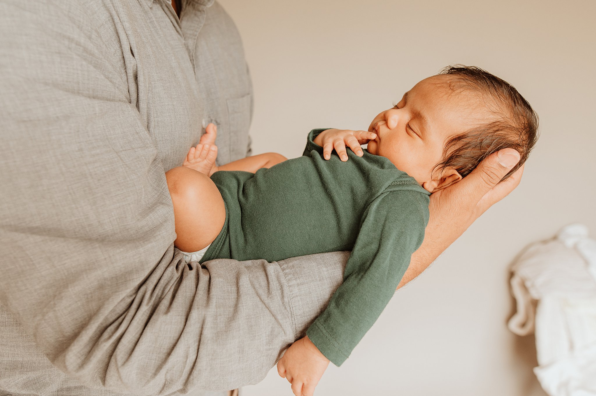 A newborn baby in a green onesie sleeps in dad's arm while he stands thanks to a prenatal chiropractor vancouver