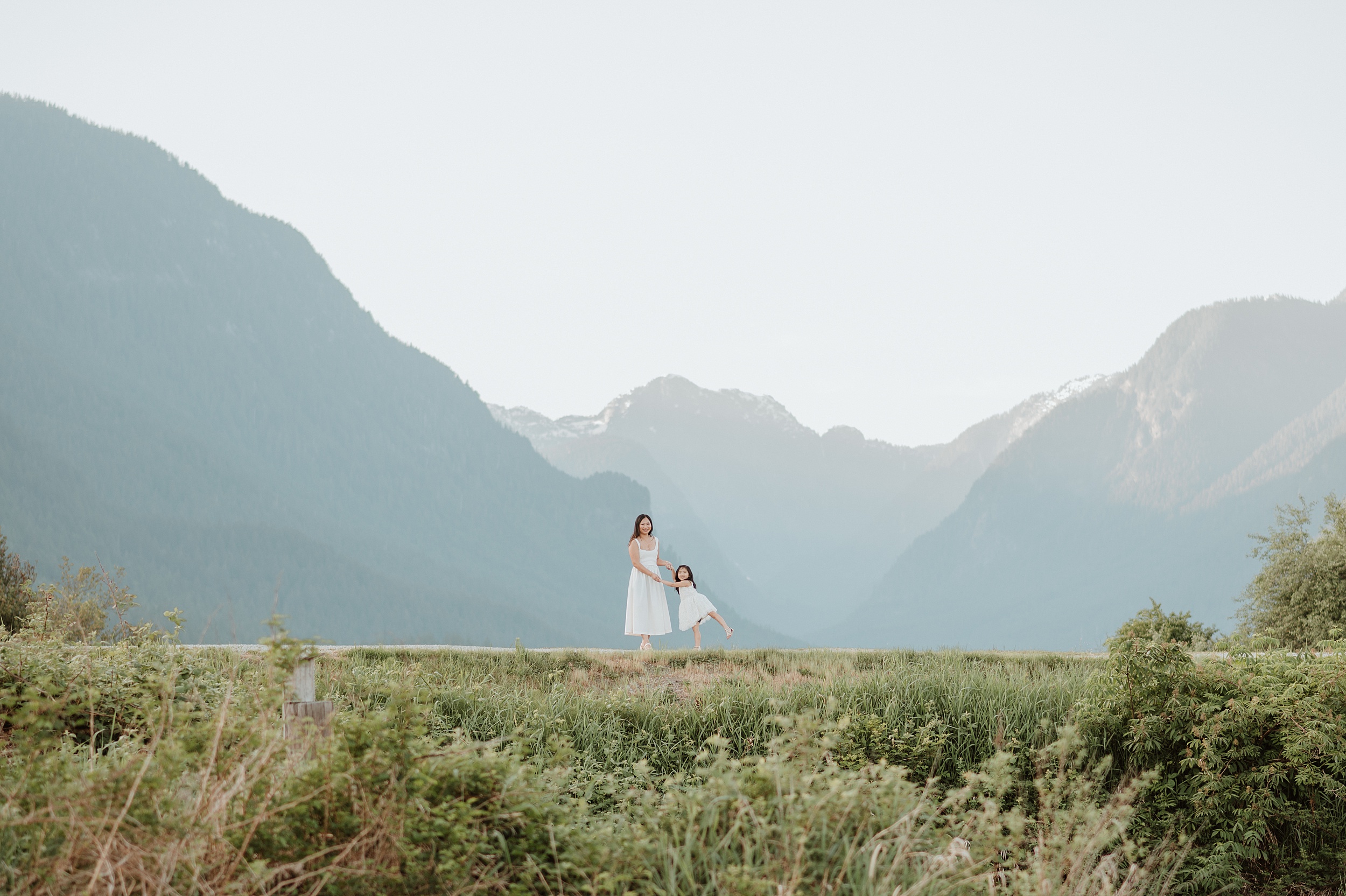 A mother and toddler daughter dance on a scenic park trail in white dresses holding hands before visiting vancouver playgrounds