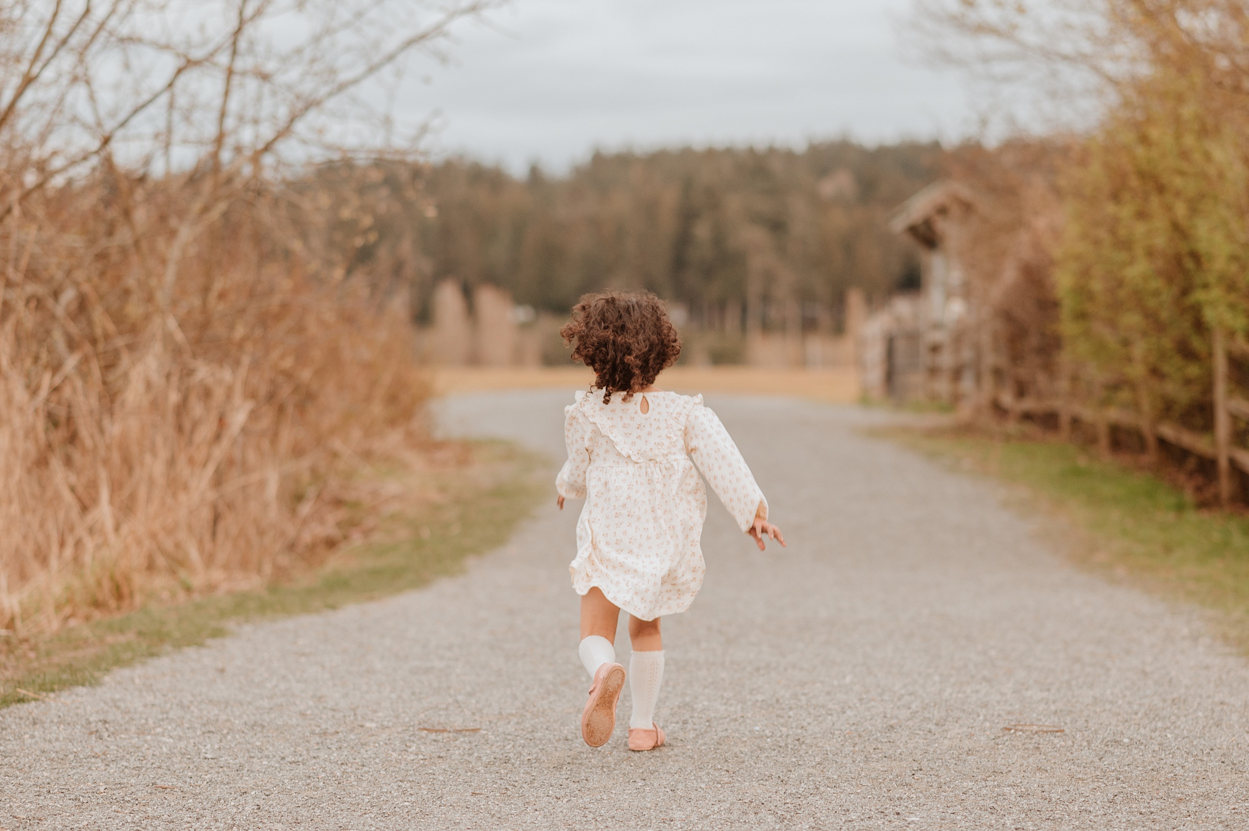 A toddler girl in a white dress runs down a park sidewalk at sunset after meeting an au pair vancouver