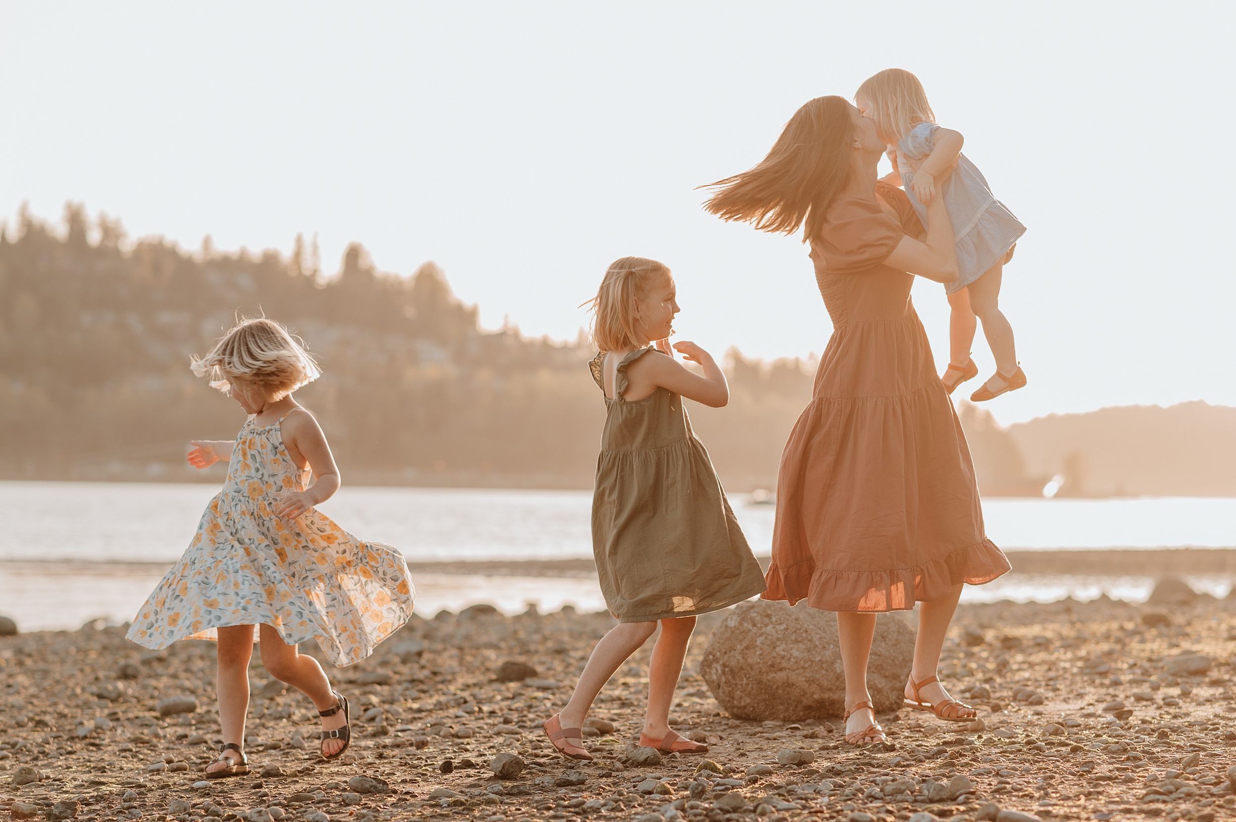 A mother plays and dances with her three toddler daughters on a beach at sunset after visiting Child Therapists In Vancouver