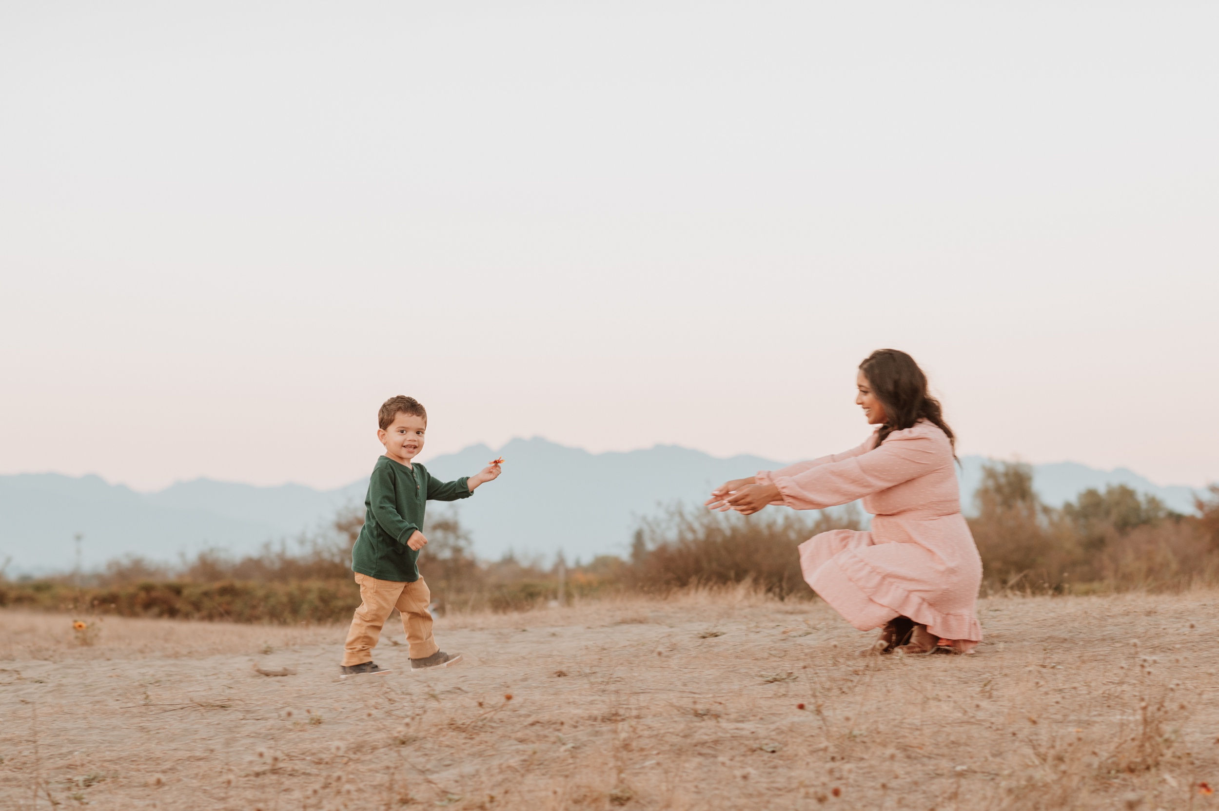 A toddler boy excitedly shows mom a wildflower while walking towards her after staying at kid friendly hotels vancouver