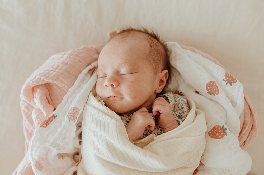 A newborn baby sleeps in a bundle of blankets on a bed after meeting mamamilk