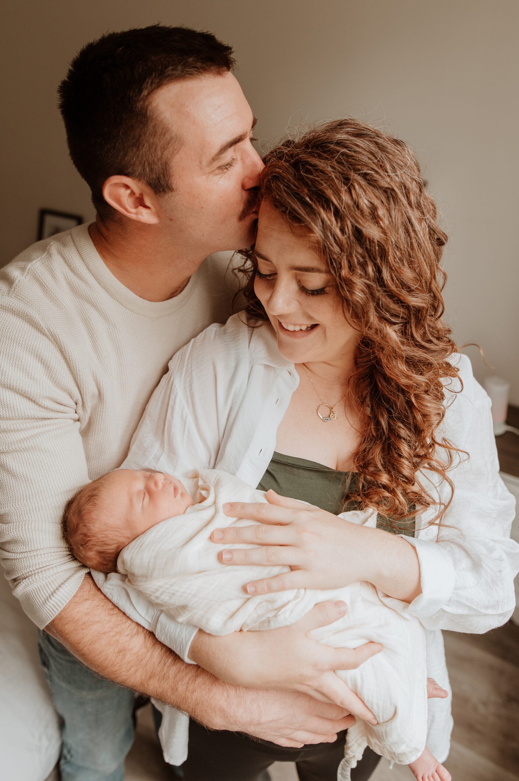 A happy mom cradles her sleeping newborn as dad kisses her head