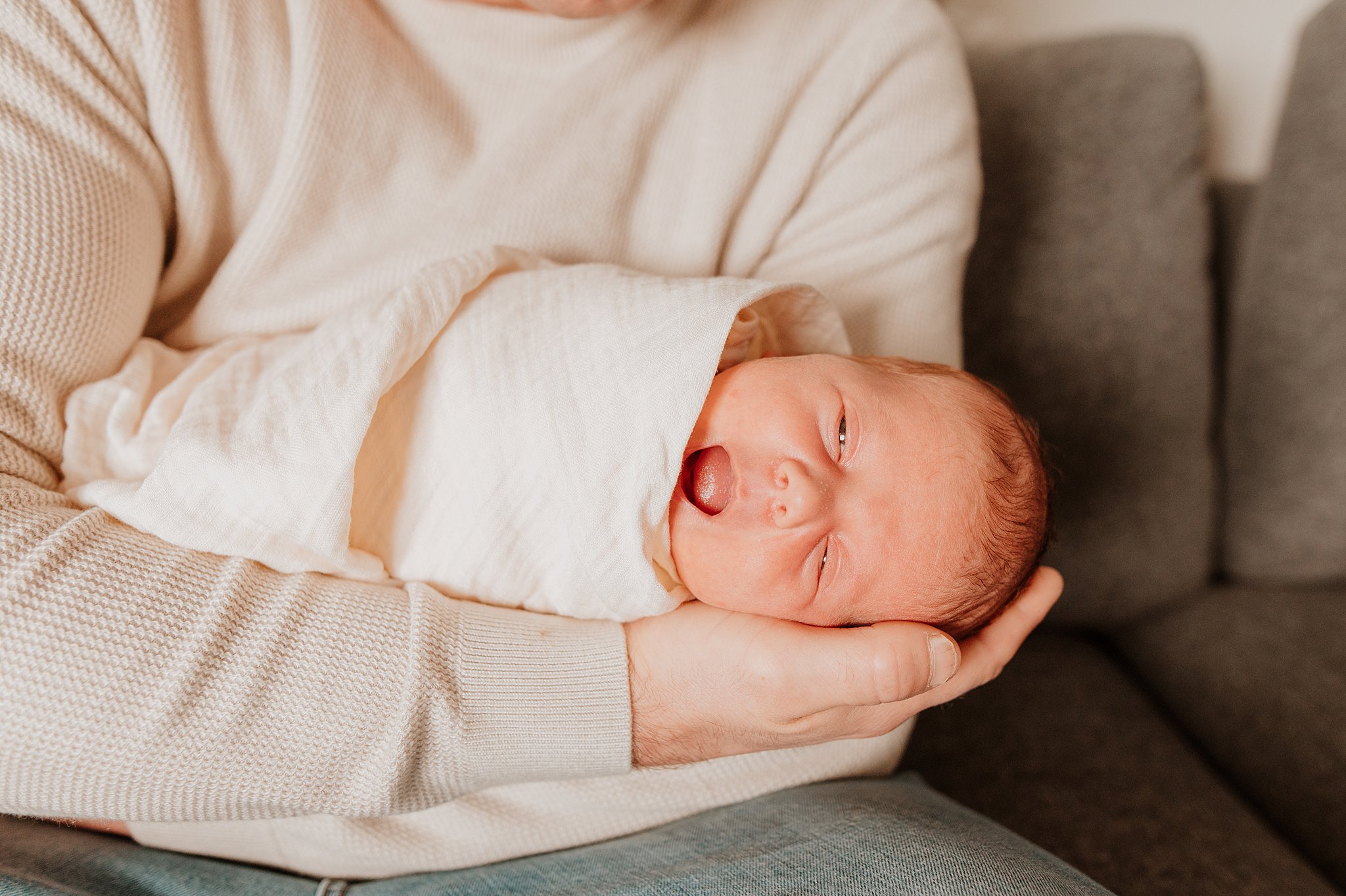 A newborn baby yawns while laying in dad's lap after meeting with Nooks and Nannies