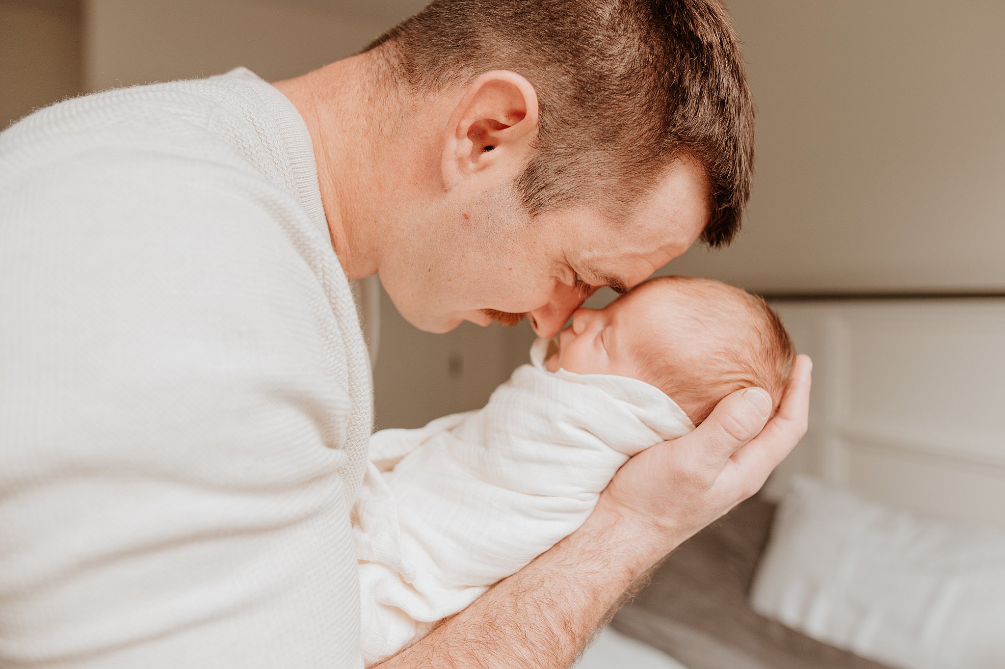 A happy new dad snuggles foreheads with his sleeping newborn baby after meeting Nooks and Nannies