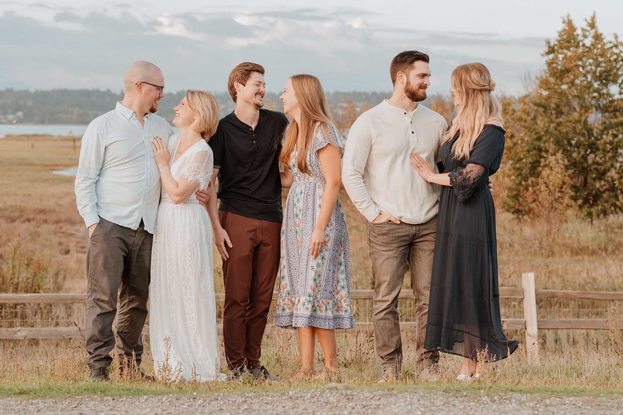 Three young couples stand smiling at each other on a hill at sunset