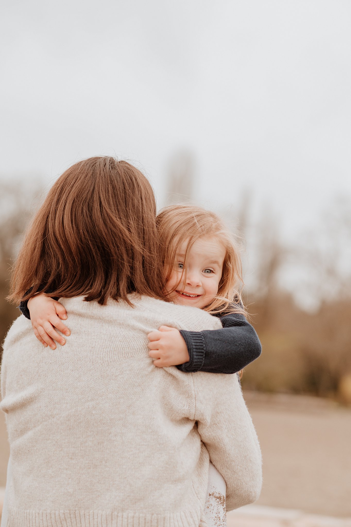 A smiling toddler hugs onto mom while peeking over her shoulder after meeting with diamond personnel vancouver