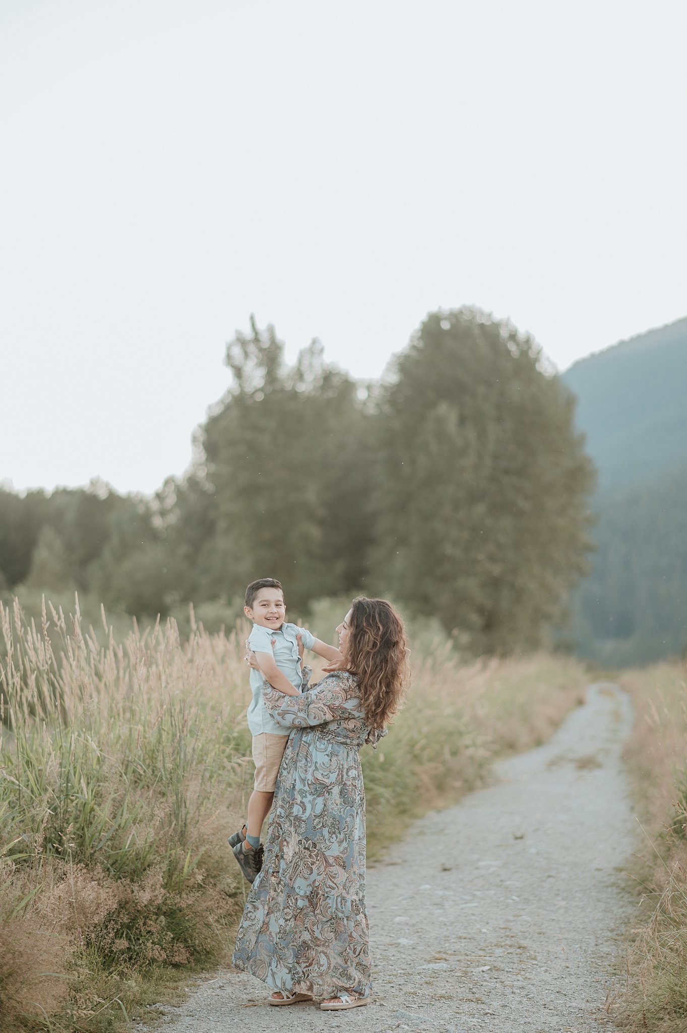 A mother lifts her laughing toddler son on a hiking trail at sunset after visiting dilly dally kids