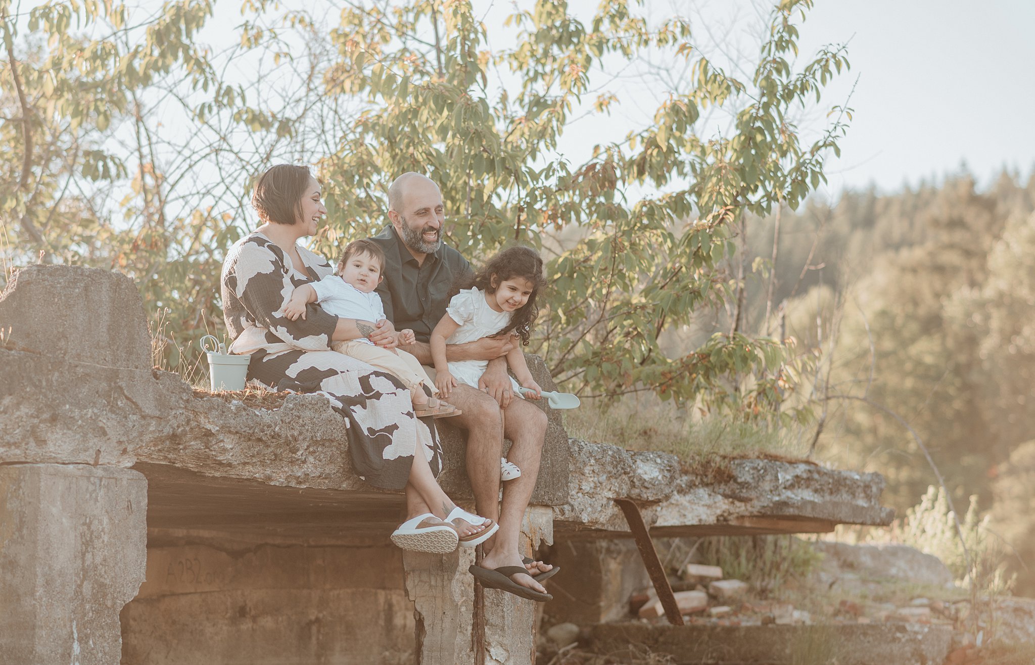 A happy family of 4 sit on a ledge in a park while playing after visiting sweet monkey vancouver