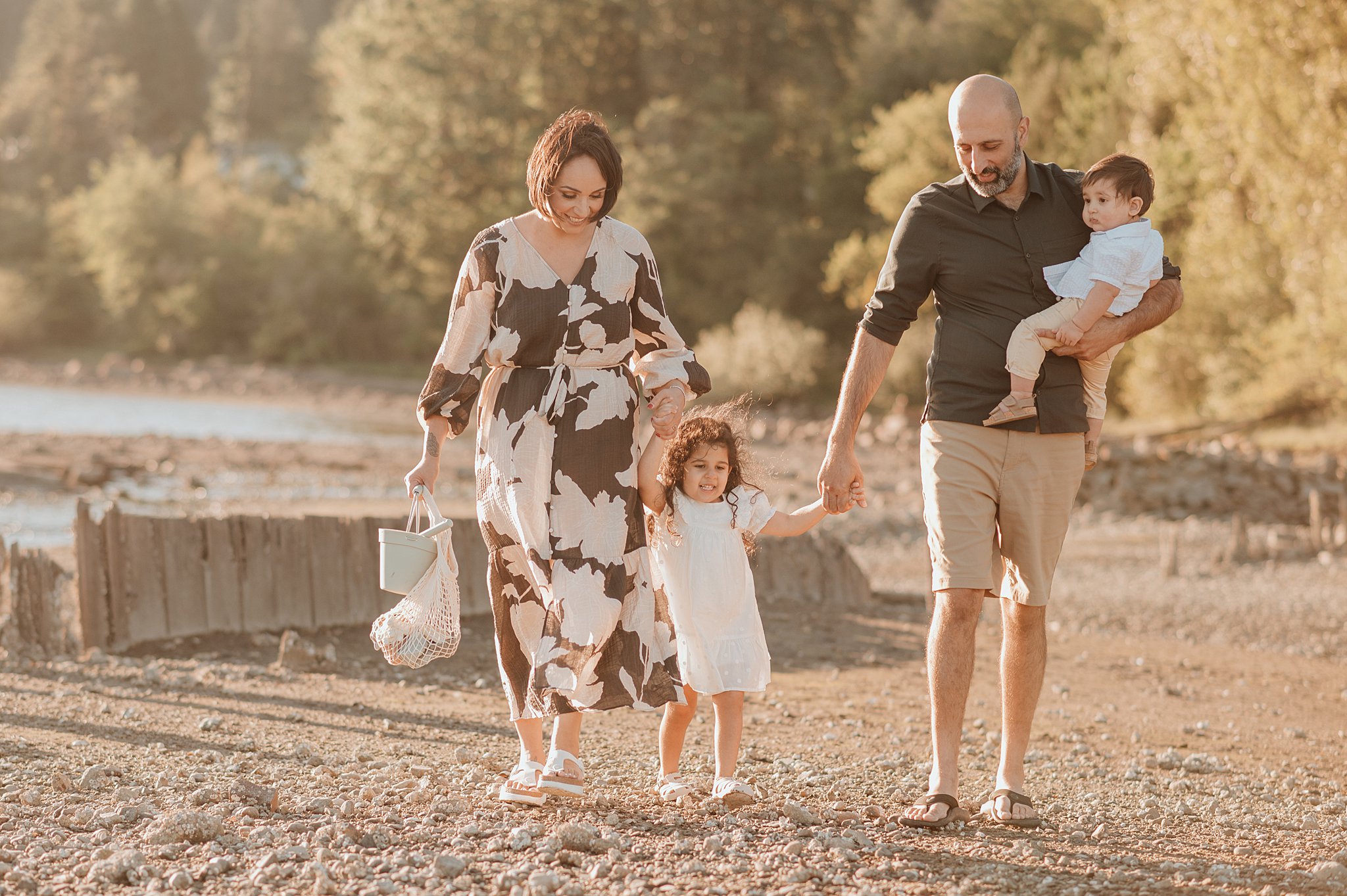 A mom and dad walk on a beach holdinghands with their toddler daughter on the way to play after visiting sweet monkey vancouver