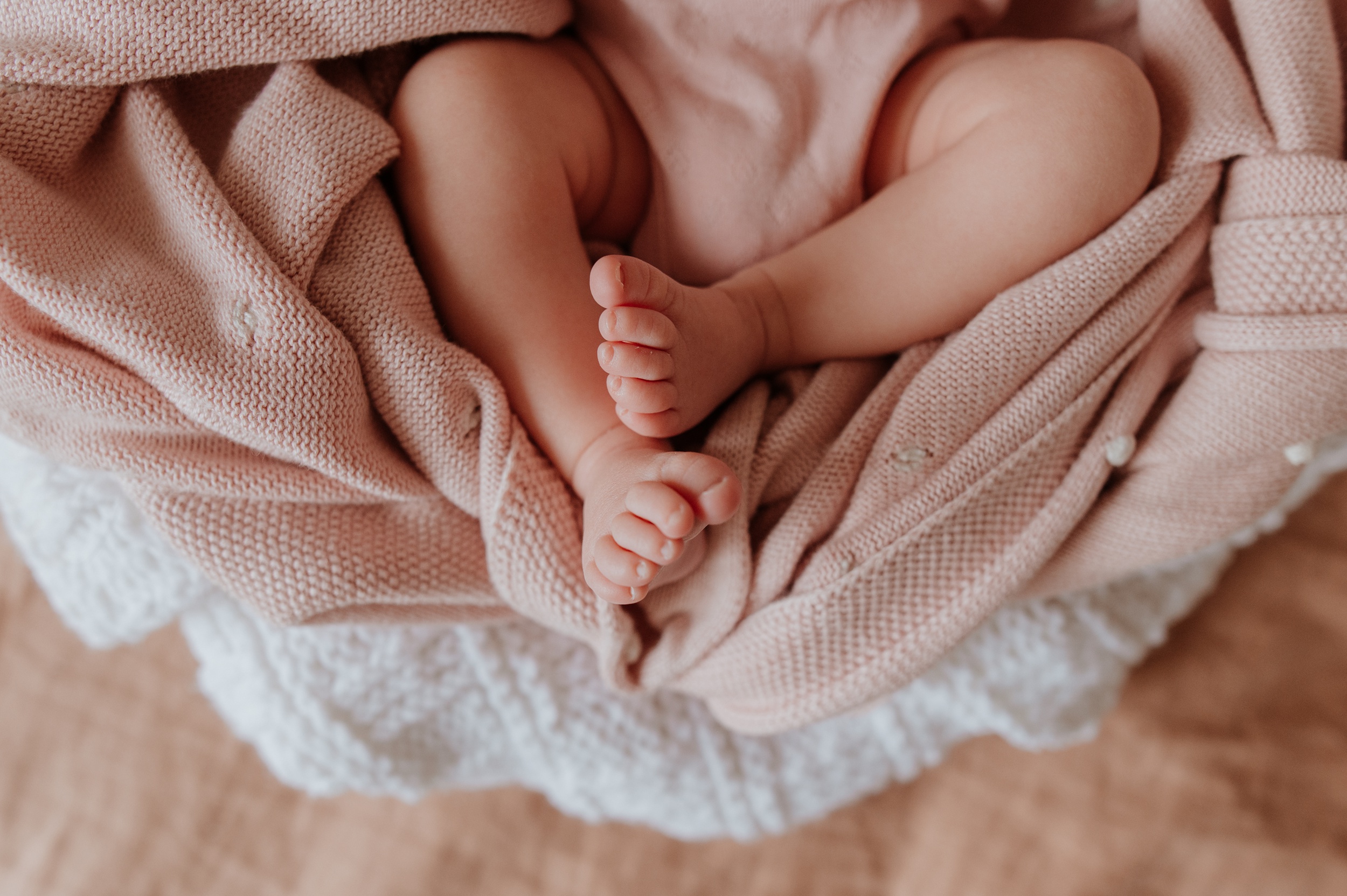 Details of a sleeping newborn baby's feet and legs in a pink blanket