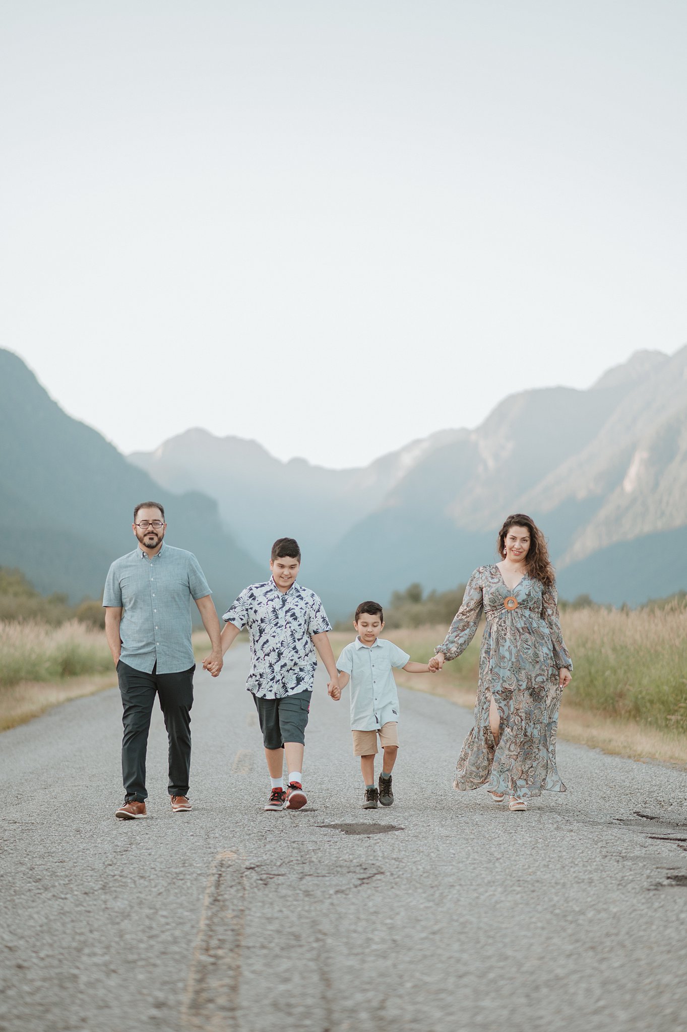 A happy family of 4 with 2 young boys walk hand in hand down a rural street in the mountains after west side family place