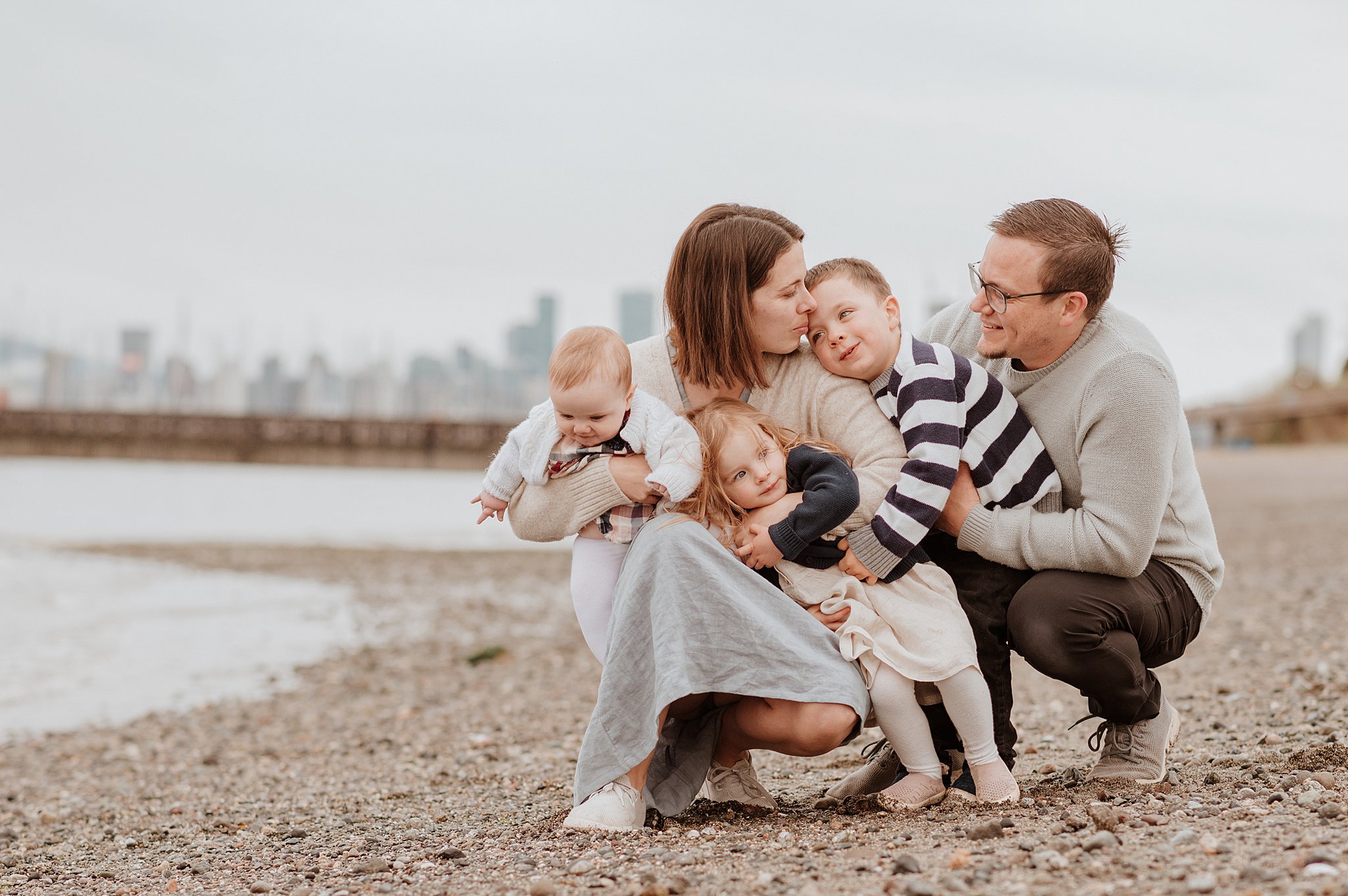 A happy family of 5 with 3 babies hugs on a beach after visiting kaboodles toy store