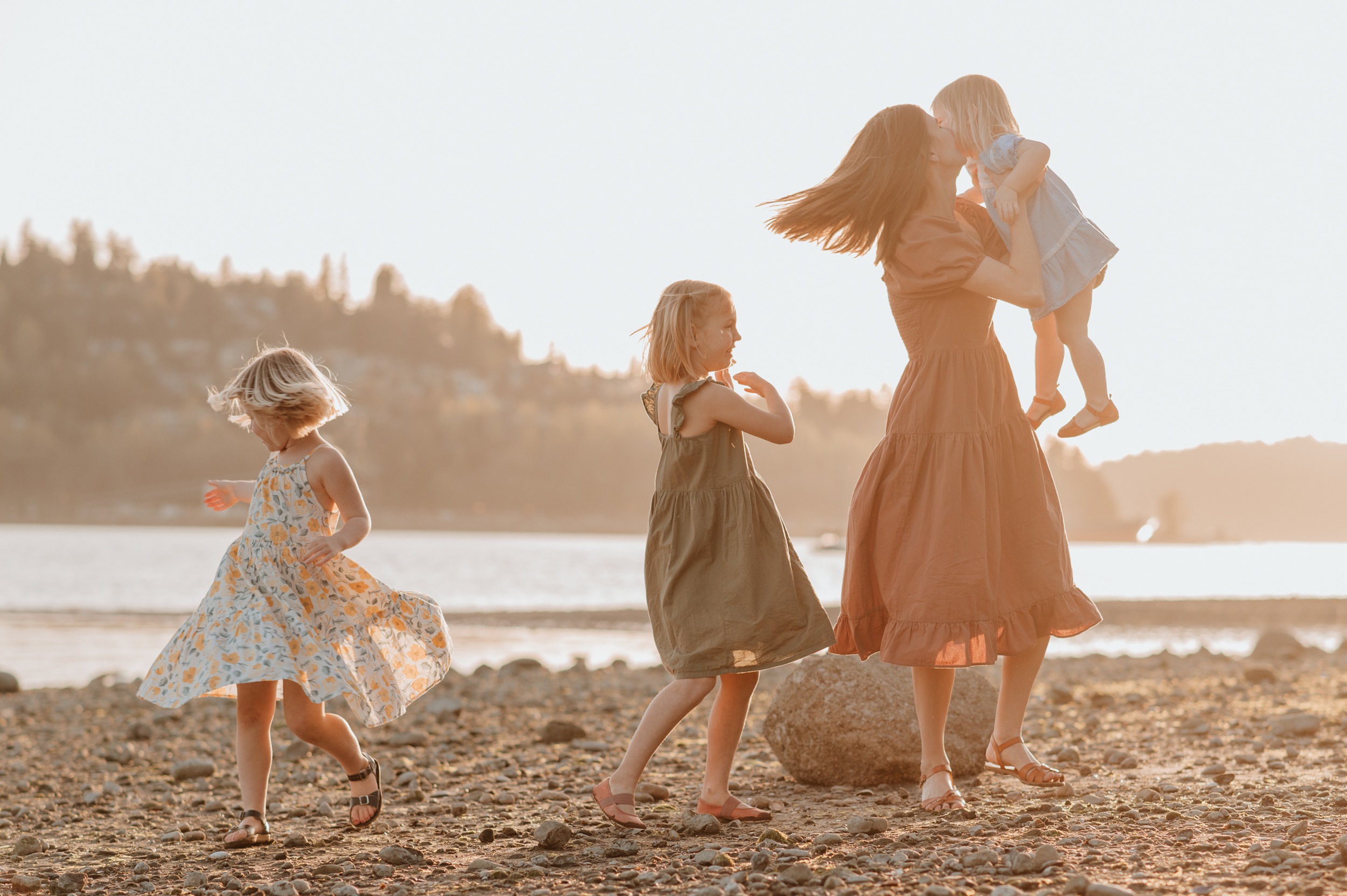 A mom dances and plays with her three young daughters on a beach at sunset