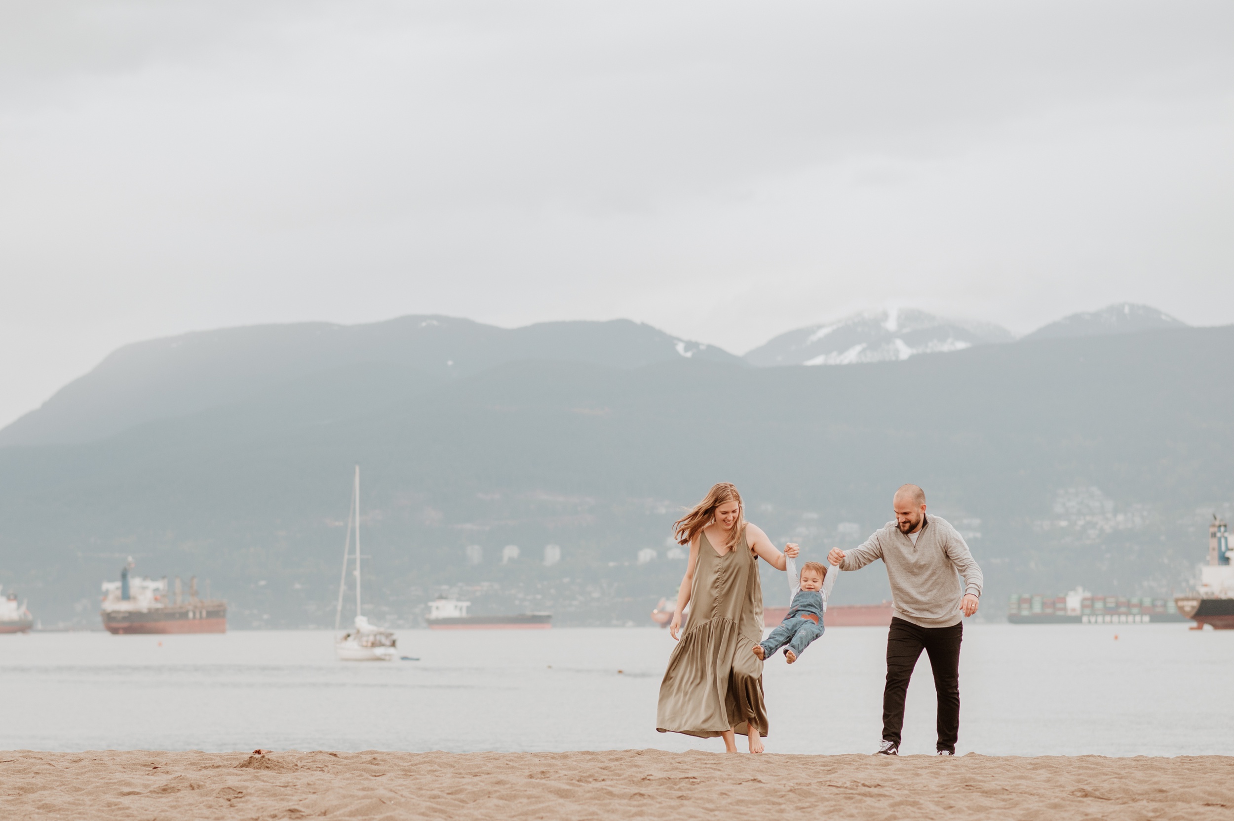 A toddler swings while holding mom and dad's hands on a beach after visiting hip baby vancouver