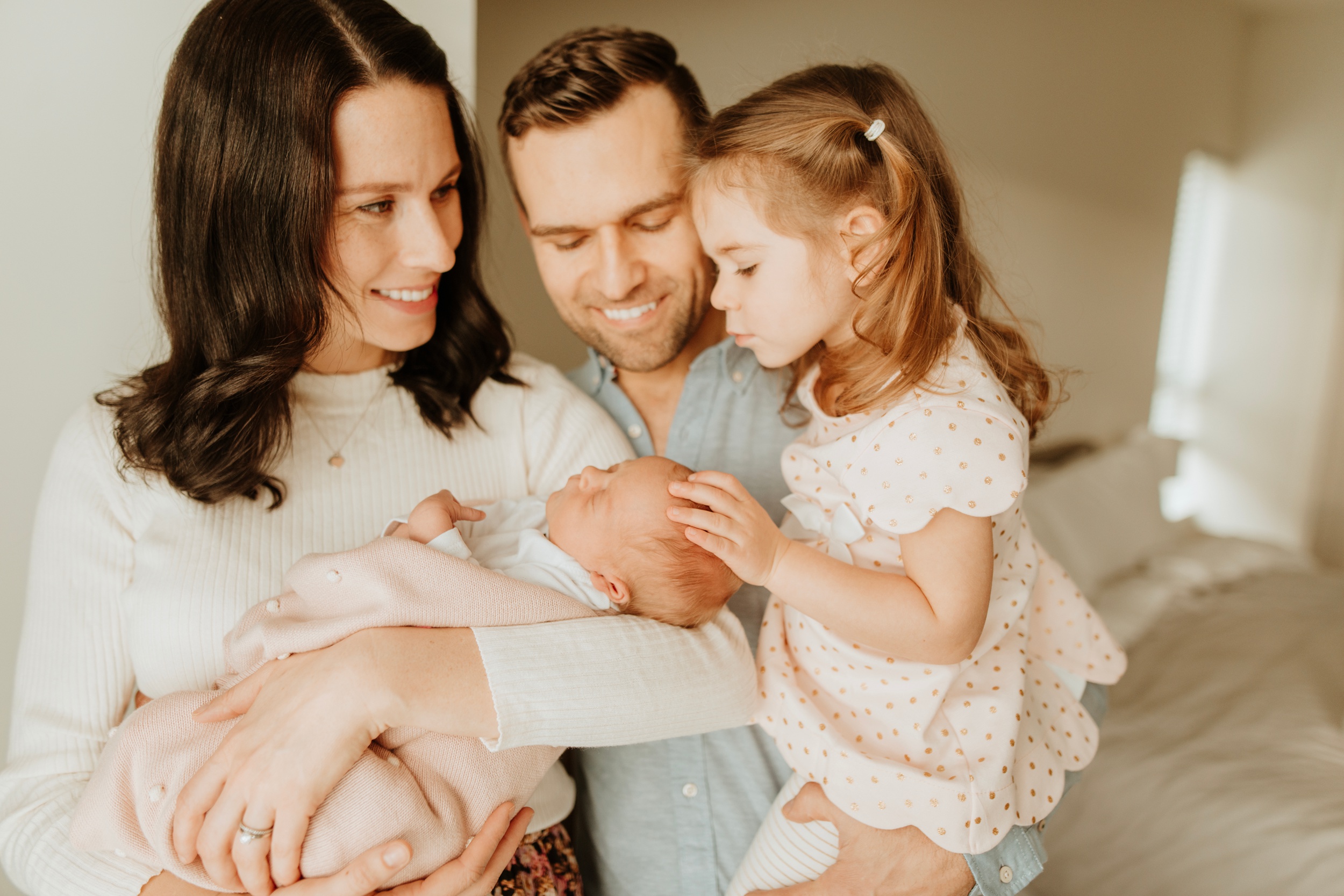 A young girl caresses her sleeping newborn sibling in mom's arms