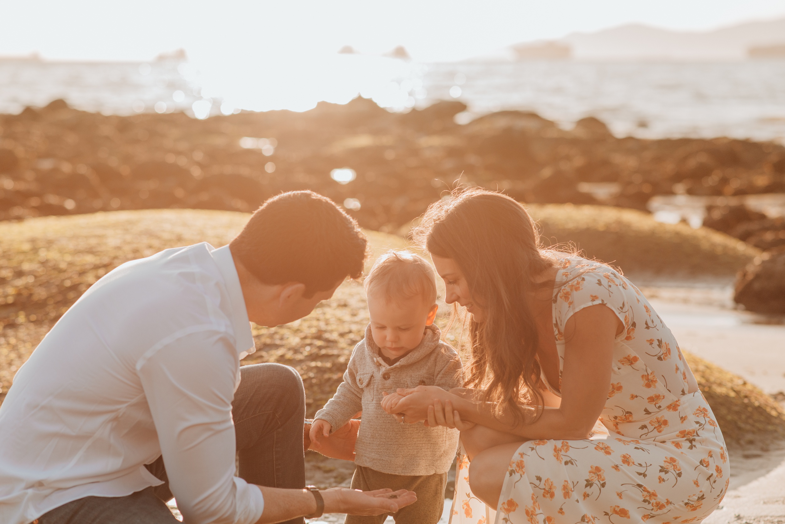 A toddler in a sweater explores a beach with mom and dad at sunset after visiting lilly and frank