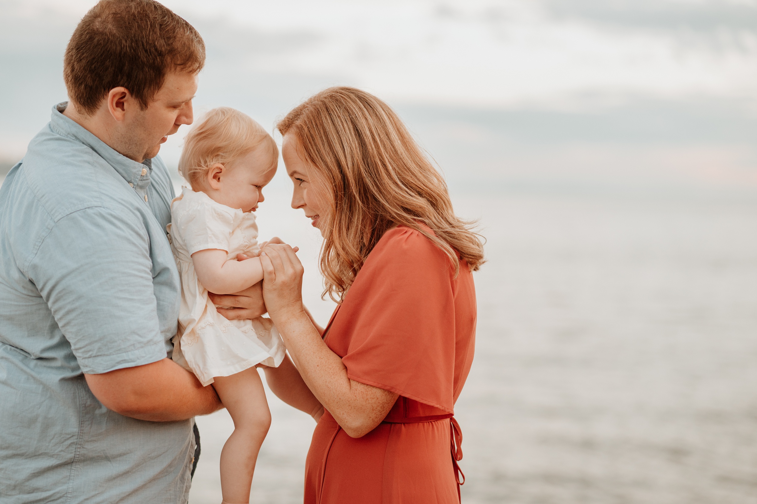 Happy mom and dad in red and blue play with their daughter by the water