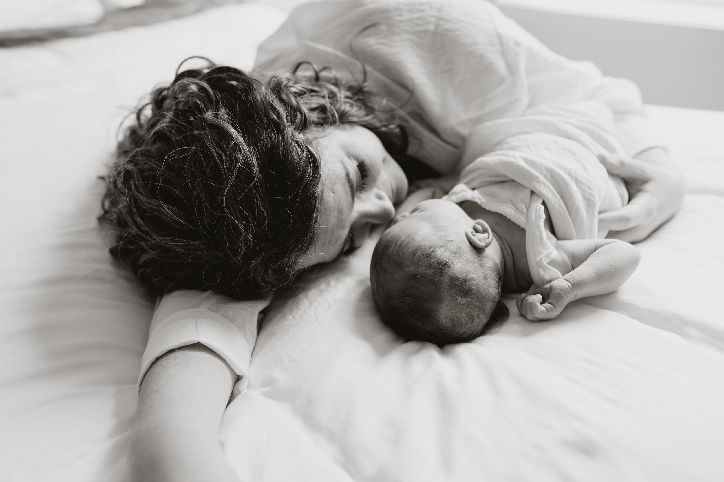 A new mom snuggles on a bed with her newborn in black and white after a prenatal massage in Langley, BC