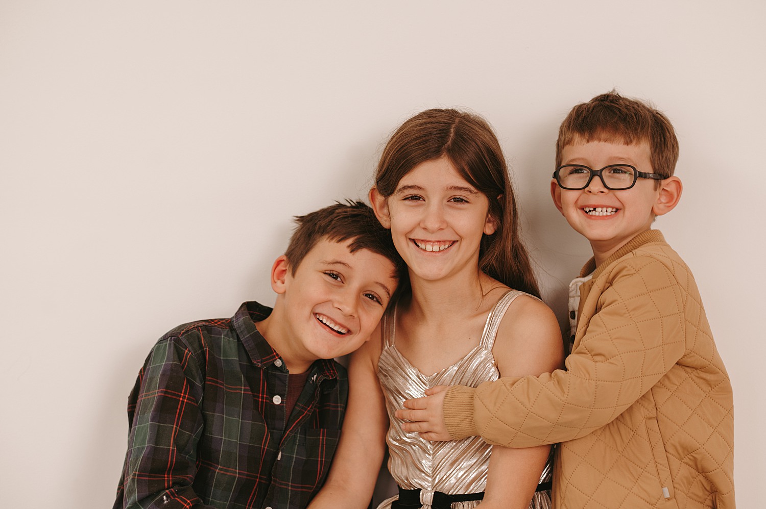 Studio family photographer capturing warm, natural portraits of an older sister and her two little brothers