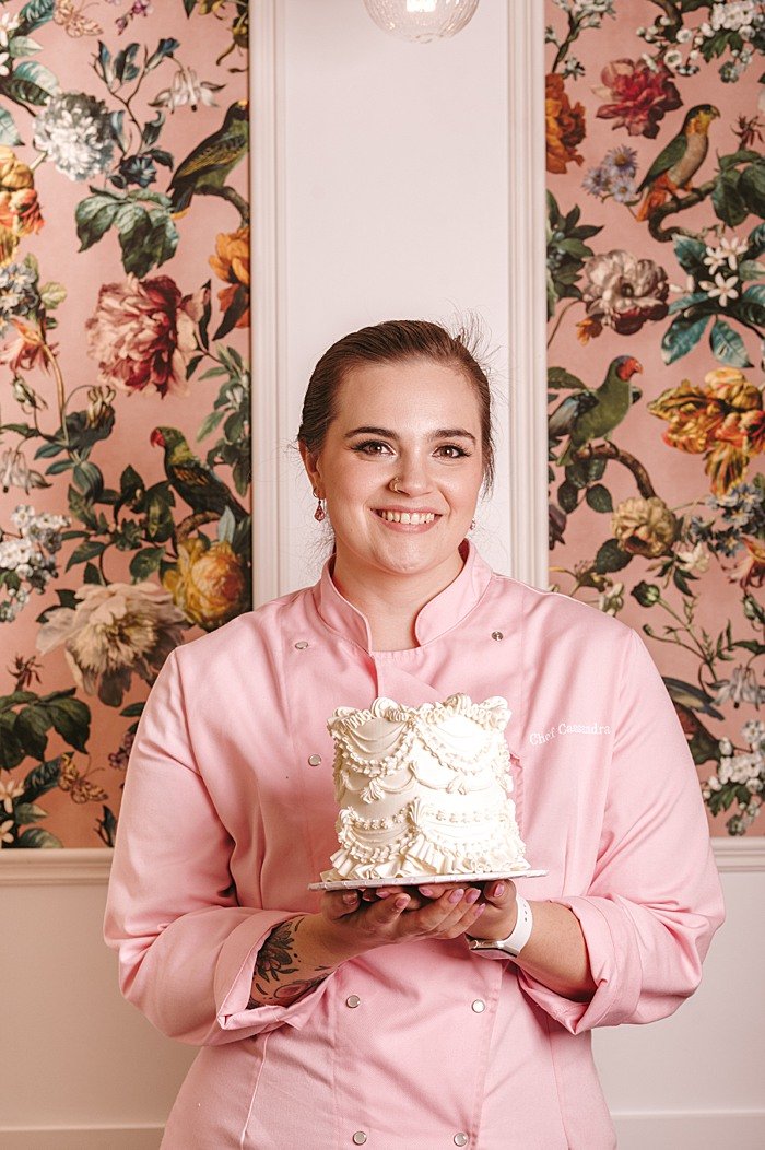 Business portrait of a cake maker holding a beautiful cake in her cafe